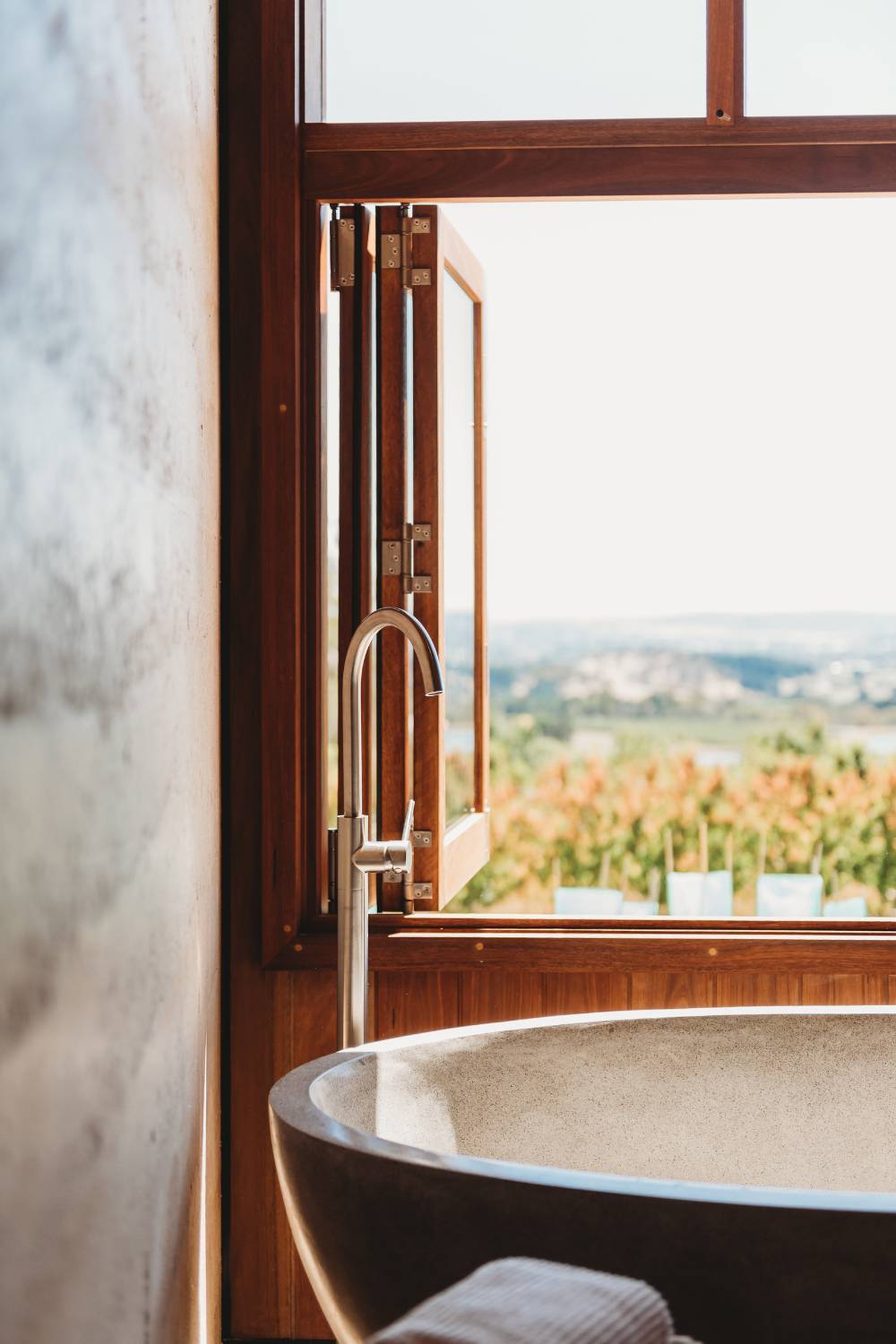 An inviting scene showcasing a bathtub positioned next to a window with a breathtaking view of Orange, New South Wales. The image captures the luxurious ambiance of the setting, with the bathtub elegantly adorned and the window framing a stunning vista of rolling hills and verdant landscapes.