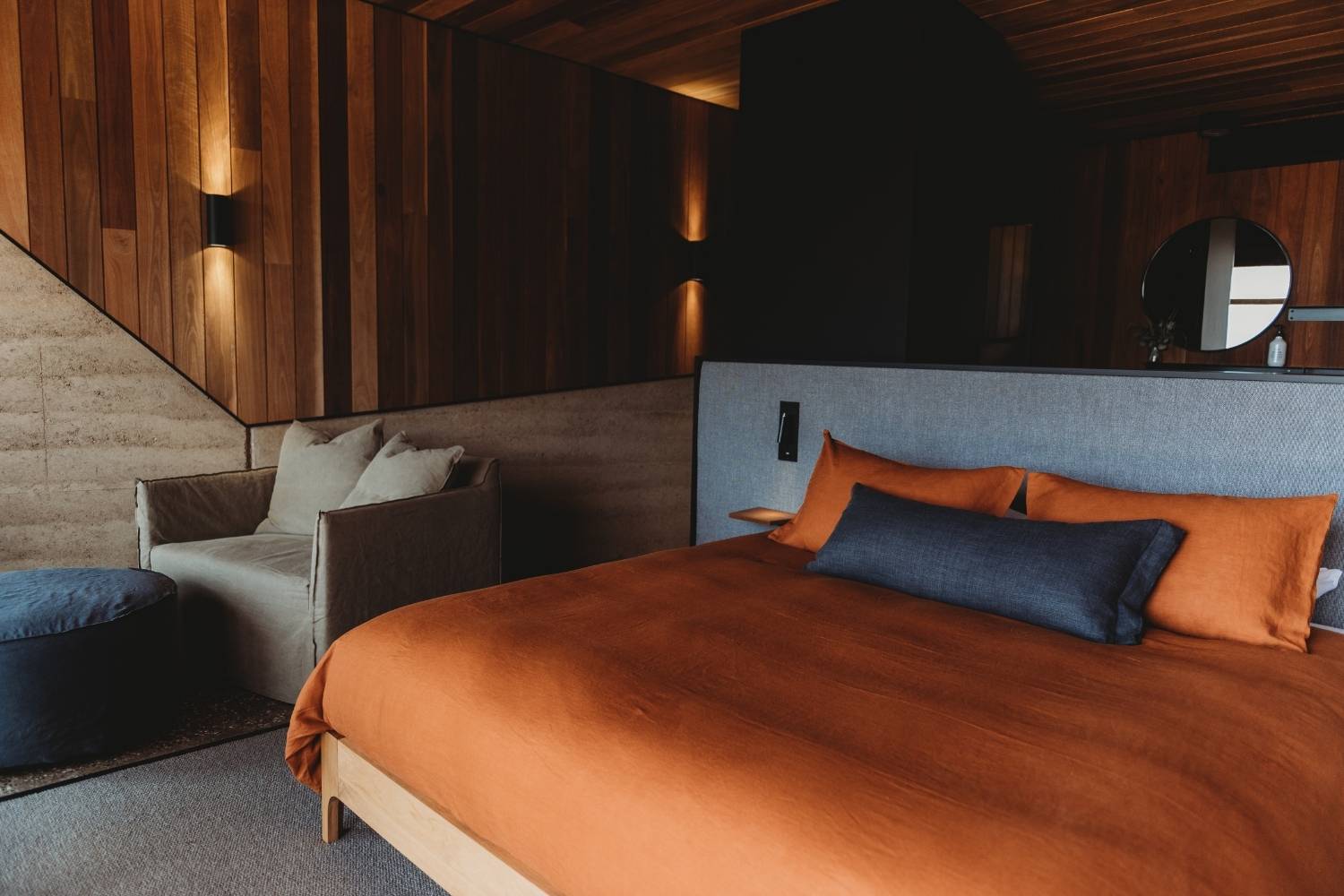 An image of a bed dressed in rich orange linen, illuminated by warm and dim lighting. The vibrant orange hue of the bedding adds a pop of color and warmth to the space, creating a cozy and inviting atmosphere. 